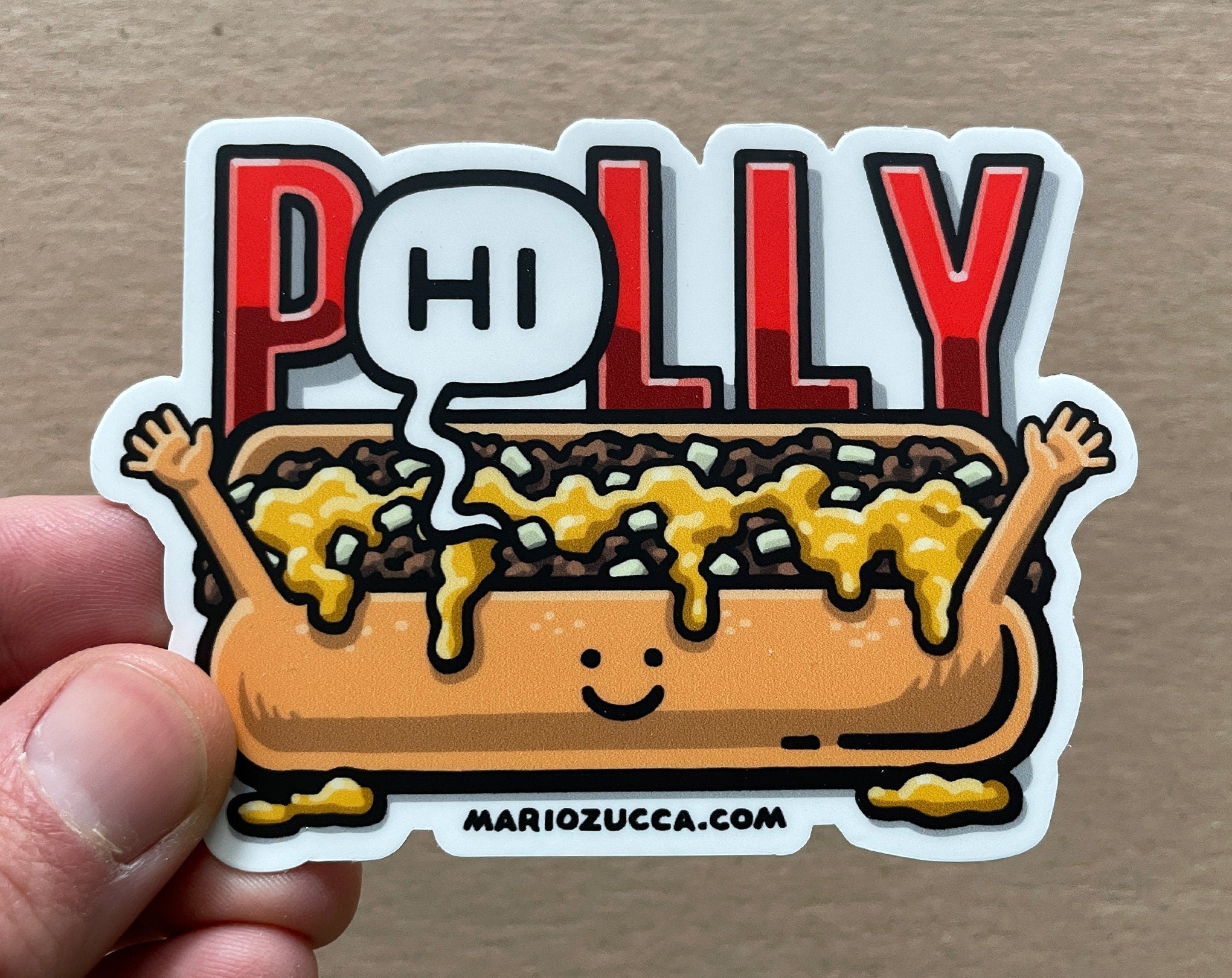 Sticker of a hot dog with mustard and a speech bubble saying 'Polly' held by a hand on a brown background.